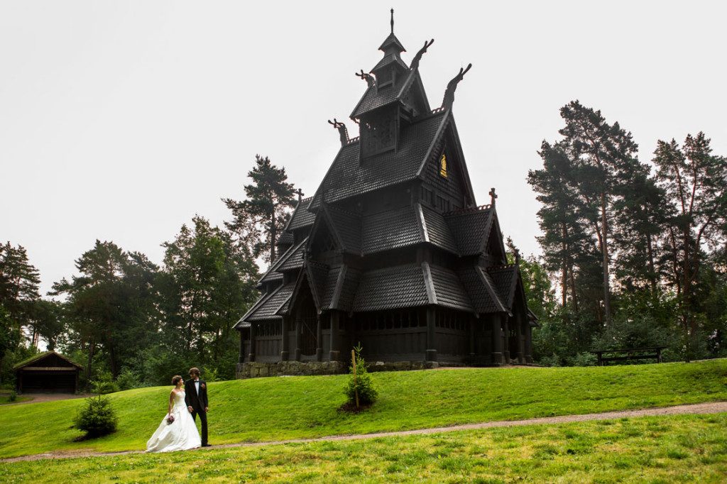 Stavkirken på Norsk Folkemuseum med brudepar på stien under kirken